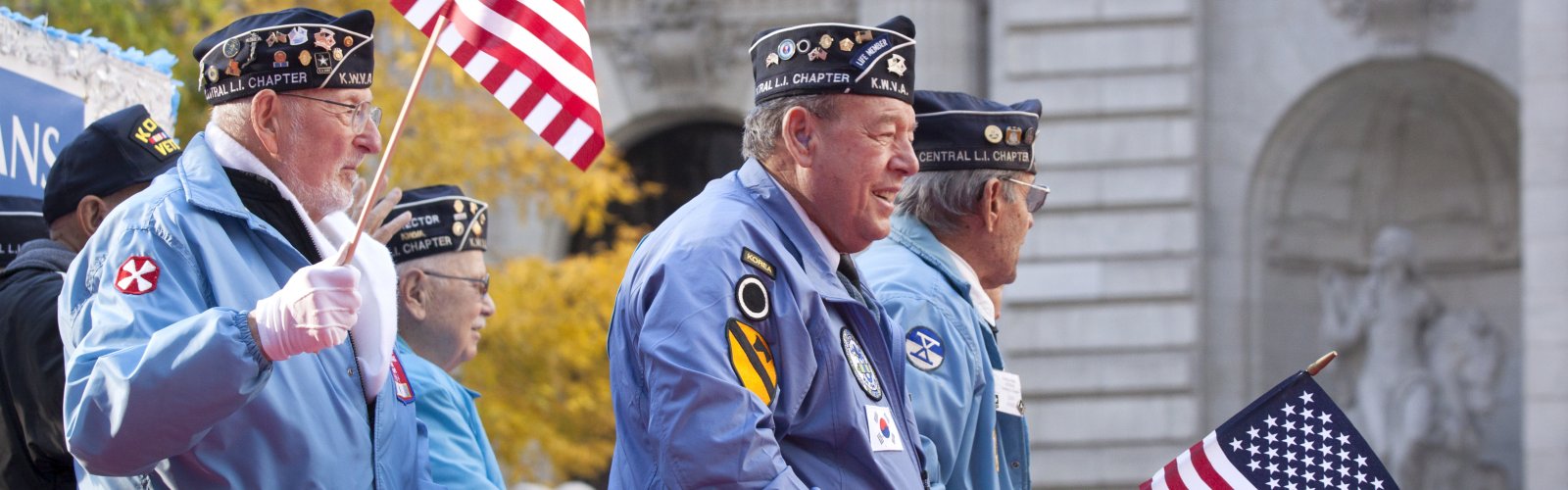 Several older men in Korean War veterans caps march in a parade