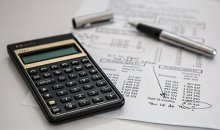 Photo of a calculator, papers and pens on a table