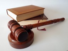 A gavel (a small wooden hammer used by judges to bring a courtroom to order) sits on a white surface in front of two stacked legal books. 