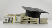 A black graduation caps on top of stacks of U.S. $100 bills.