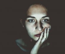 Photo credit: Niklas Hamann. A low-light photo of a concerned looking woman with her hand on her face