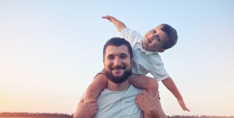 A bearded white man standing in a field, holding a young child on his shoulders