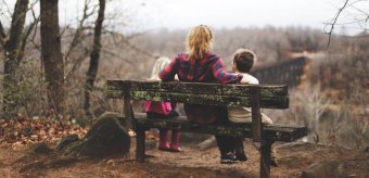 Photo credit: Benjamin Manley. A woman sits on a bench, back to the camera, with her arms around two small children