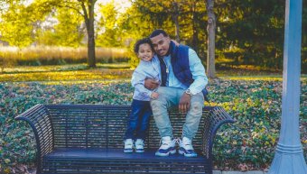 Photo credit Chris Benson. A young black man sitting on a bench embracing a young child