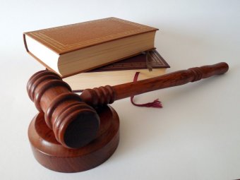 A gavel (a small wooden hammer used by judges to bring a courtroom to order) sits on a white surface in front of two stacked legal books.