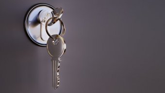 A close up of a silver key, hanging from another key in lock.