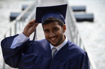 Photo credit: Muhammad Rizwan. A young man wearing a graduation cap and gown smiles at the camera.