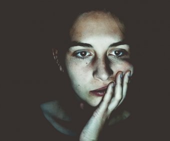 Photo credit: Niklas Hamann. A low-light photo of a concerned looking woman with her hand on her face