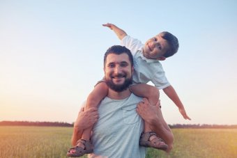 A bearded white man standing in a field, holding a young child on his shoulders