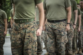 A picture of the torsos of several people wearing camoflague pants and olive drab t-shirts.