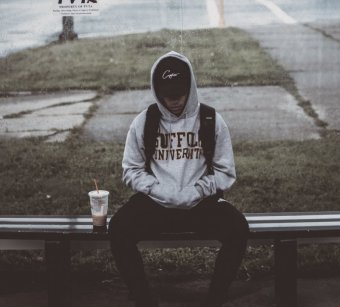 Photo credit: whereslugo. Photo of a young person in a hoodie and baseball cap sits at a bus stop.